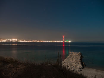 Illuminated lighthouse by sea against clear sky at night