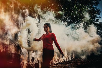Young woman standing amidst smoke in forest