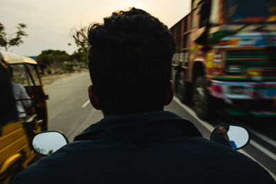 Rear view of man riding motorcycle on road during sunset