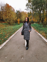 Full length portrait of young woman standing on road