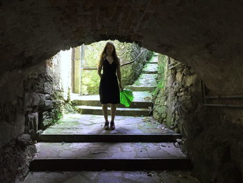 Portrait of young woman holding leaf while standing on leaf under arch