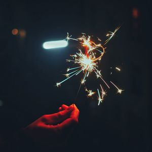 Close-up of human hand holding illuminated sparkler at night