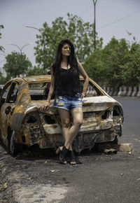 Portrait of young woman standing by abandoned car on road