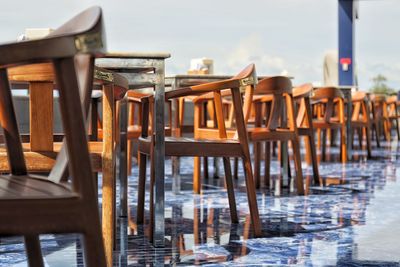 Row of wooden chairs, tables, on a shiny blue floor, al fresco dining