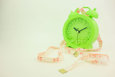 Close-up of green alarm clock with tape measure against gray background