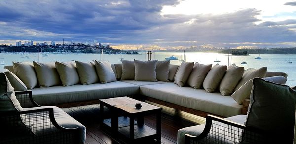 Chairs on sofa by sea against sky