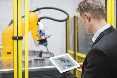 Mature businessman controlling industrial robots with digital tablet