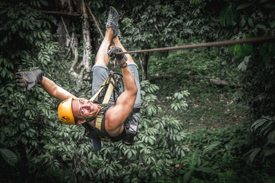 Young man hanging on rope in forest