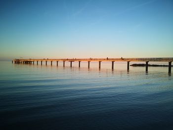 Pier over sea against clear blue sky