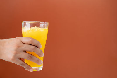 Cropped hand holding drink against yellow background