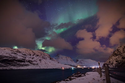 Scenic view of river and snowcapped mountains against cloudy sky at night