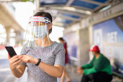Young woman wearing face shield while using mobile outdoors