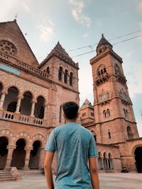 Rear view of man walking by historic building against sky