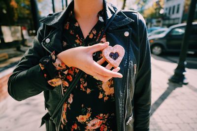 Midsection of woman holding heart shape cookie while standing on street