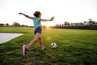 Woman playing with ball on grass against sky