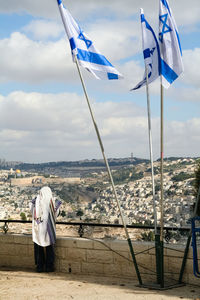 Rear view of woman standing by railing and flags against sky