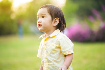 Cute boy looking away while standing on field