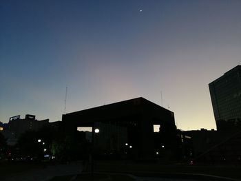 Illuminated street amidst buildings against sky at sunset