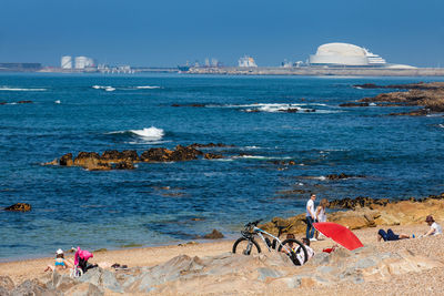 People riding bicycle by sea against sky