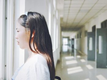 Profile view of young woman looking through window in corridor