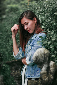 Young woman looking down while standing against plants