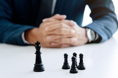 Midsection of businessman sitting by chess pieces at table