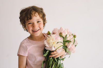 Cheerful happy child with peonys bouquet. smiling little boy on white background.