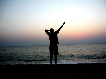 Silhouette man standing on shore at beach against sky during sunset