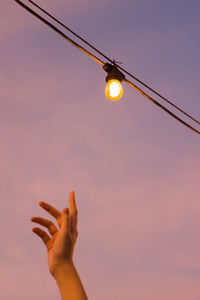 Low angle view of hand holding light bulb against sky during sunset