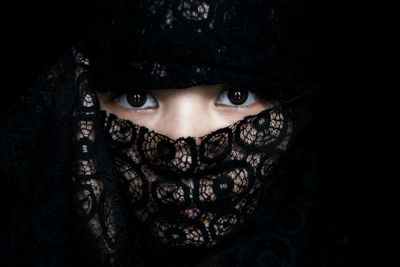 Portrait of young woman with scarf covering face against black background