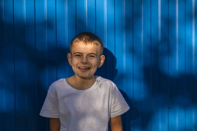 Little small happy boy 10 years old in white casual t-shirt smiling on plain blue background