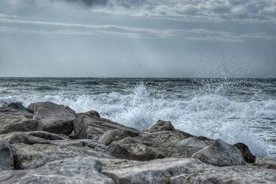 Waves splashing on rocks at shore against sky