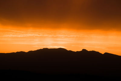 Scenic view of silhouette mountains against orange sky