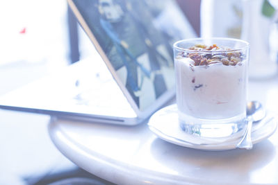 Close-up of granola in yoghurt served on table with laptop at cafe