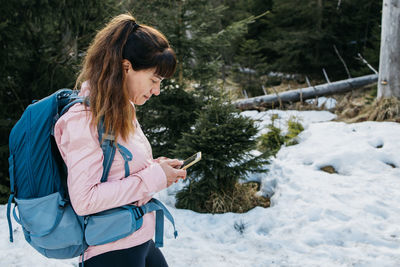 Girl with backpack on her back uses mobile phone in forest. trekking the way
