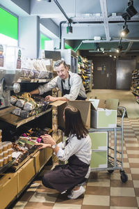 Owner looking at saleswoman while unpacking cardboard box in grocery store