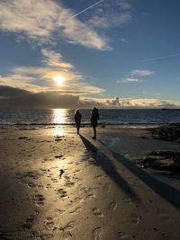 Silhouette people standing on beach against sky during sunset