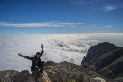 Woman sitting on rock against cloudscape