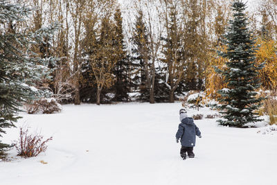 Rear view of boy walking on snow covered field in forest