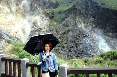Portrait of young woman with umbrella standing against mountains