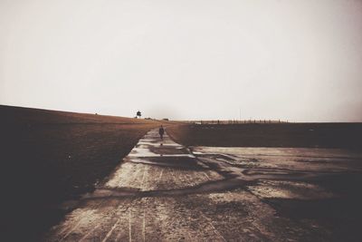 Woman standing on road amidst field against sky