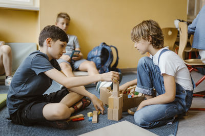 Male and female students stacking blocks while sitting on floor in school