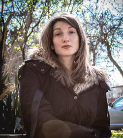 Portrait of beautiful young woman standing against trees