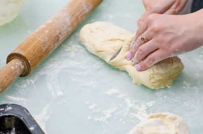 Cropped hands of woman cutting dough on marble