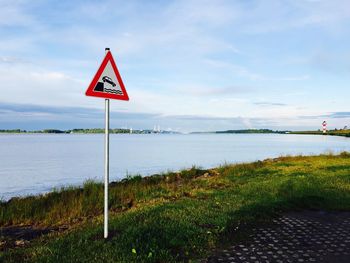 Road sign by river against sky