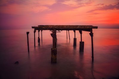 Broken pier in sea at sunset