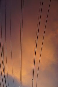 Low angle view of silhouette cables against orange sky