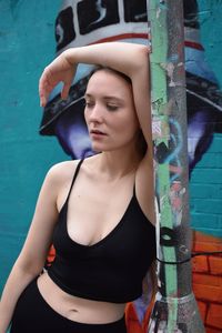 Tired young woman leaning on pole against wall