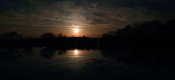 Silhouette trees by lake against sky during sunset