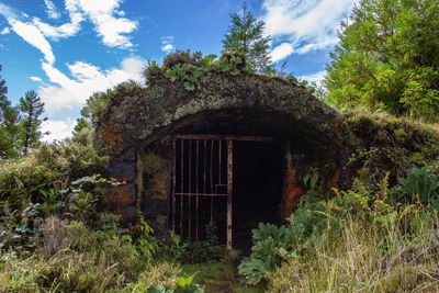 Old abandoned building by trees against sky